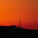 the sun is setting over a city with a radio tower in the distance