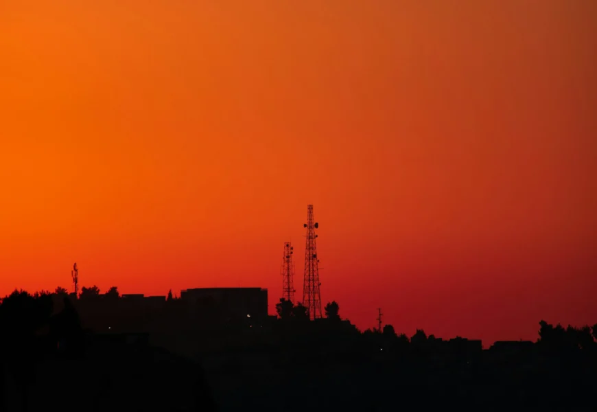 the sun is setting over a city with a radio tower in the distance