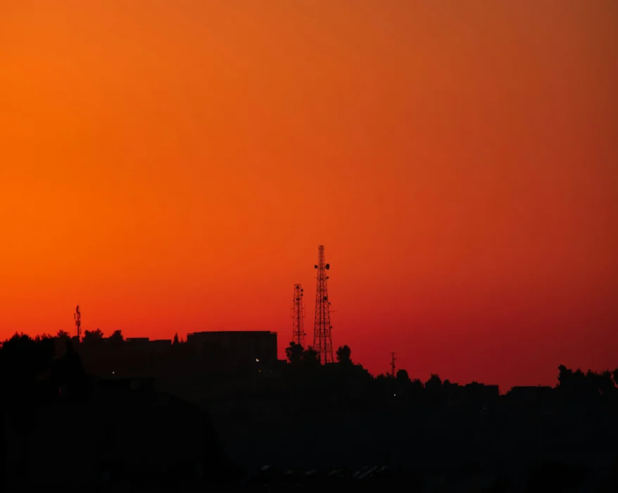 the sun is setting over a city with a radio tower in the distance