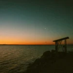 the sun is setting over the water at the beach