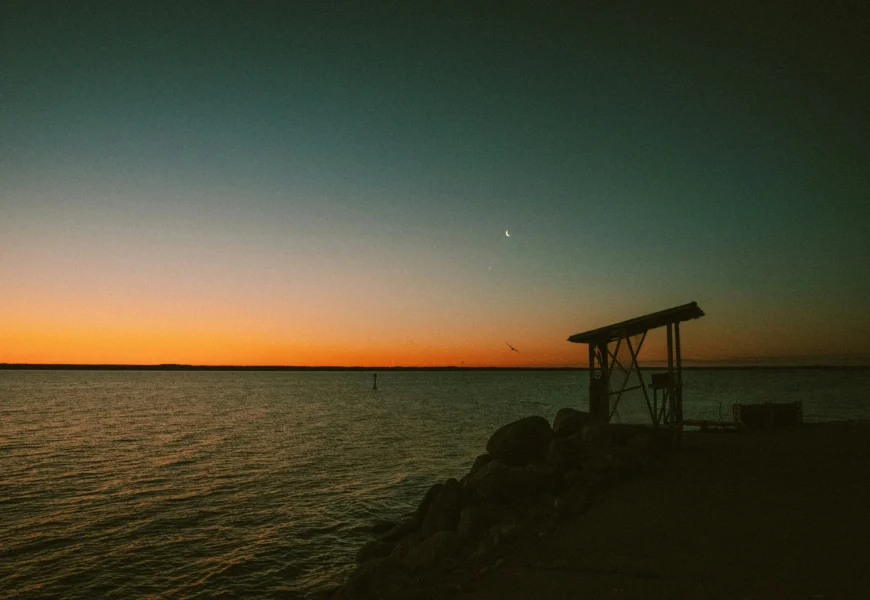 the sun is setting over the water at the beach